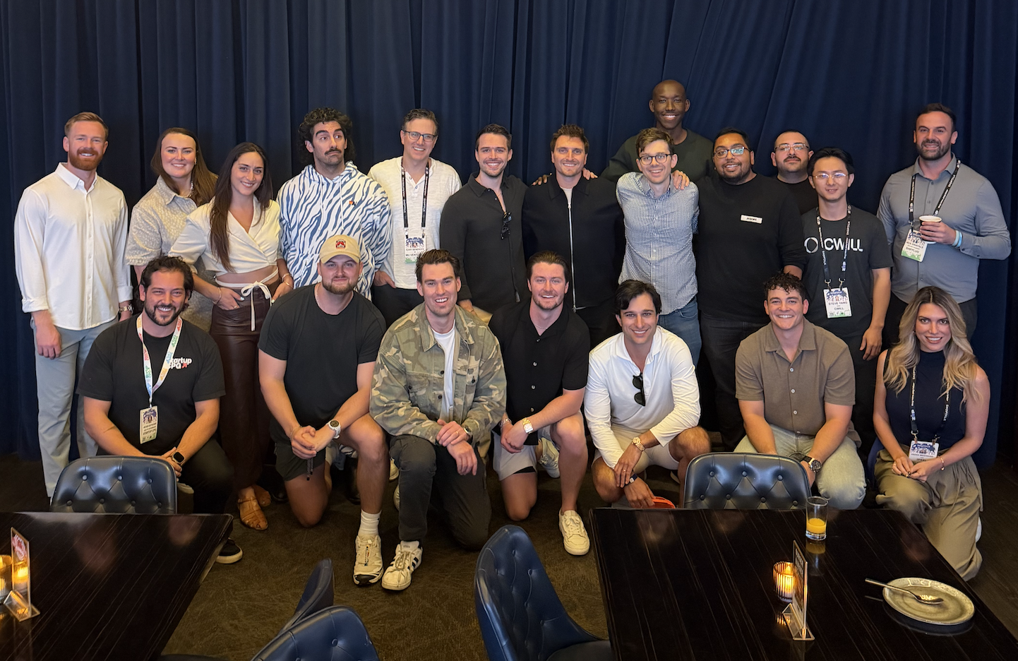 Large group photo with conference lanyards posing in two rows against a navy curtain backdrop
