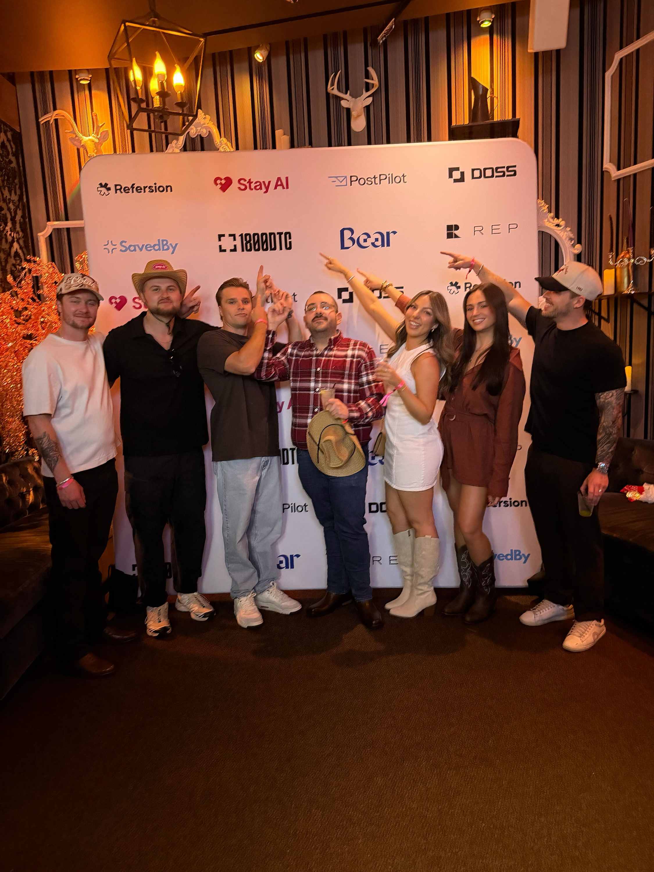 Group posing in front of a 1800DTC-branded step-and-repeat backdrop at an indoor event