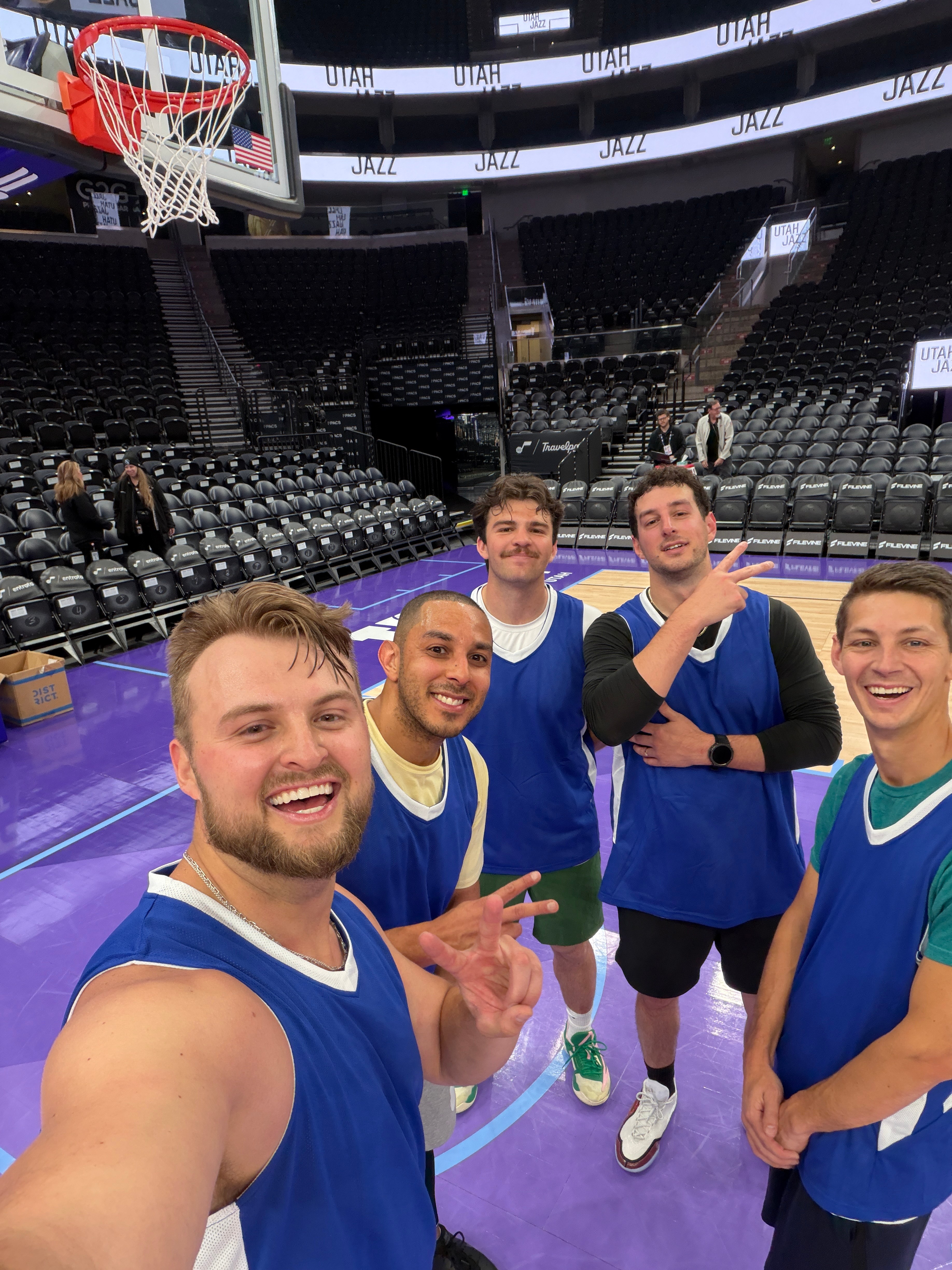 Group of friends in blue basketball jerseys taking a selfie on the Utah Jazz arena court