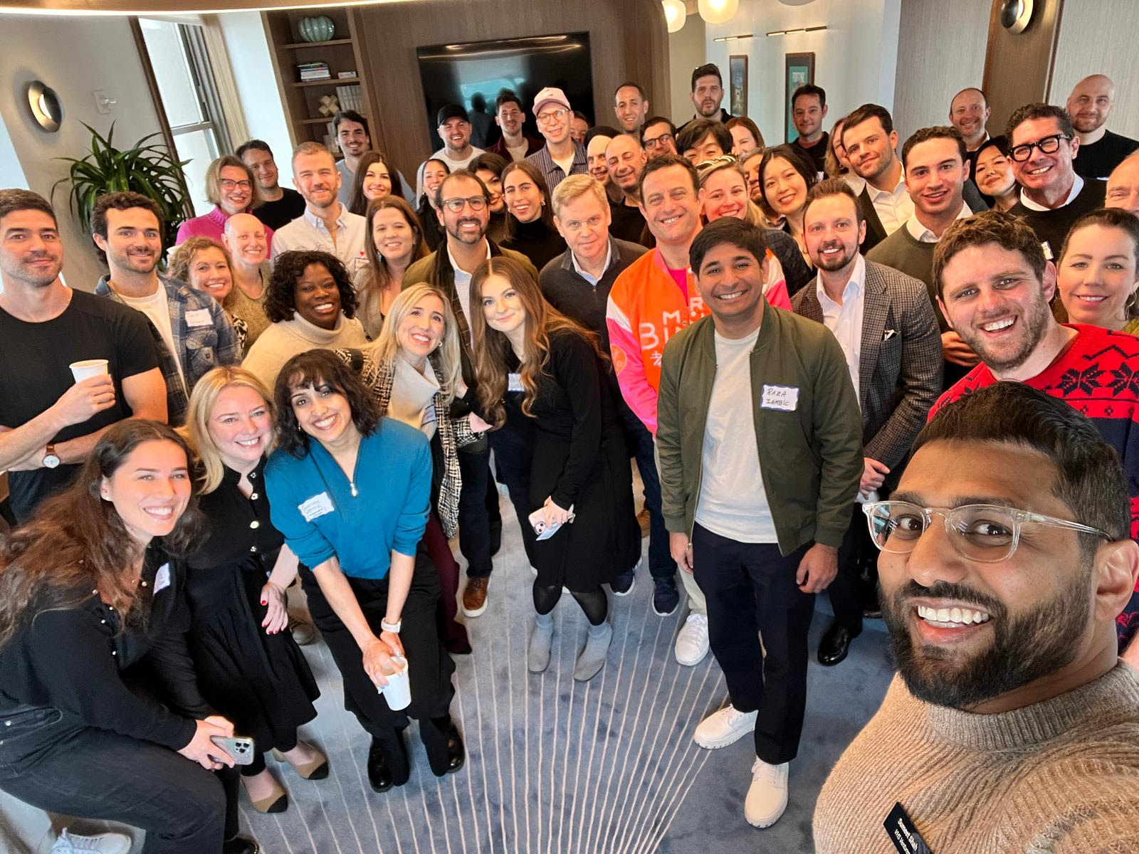 Large group selfie from above at modern apartment event space with diverse community members