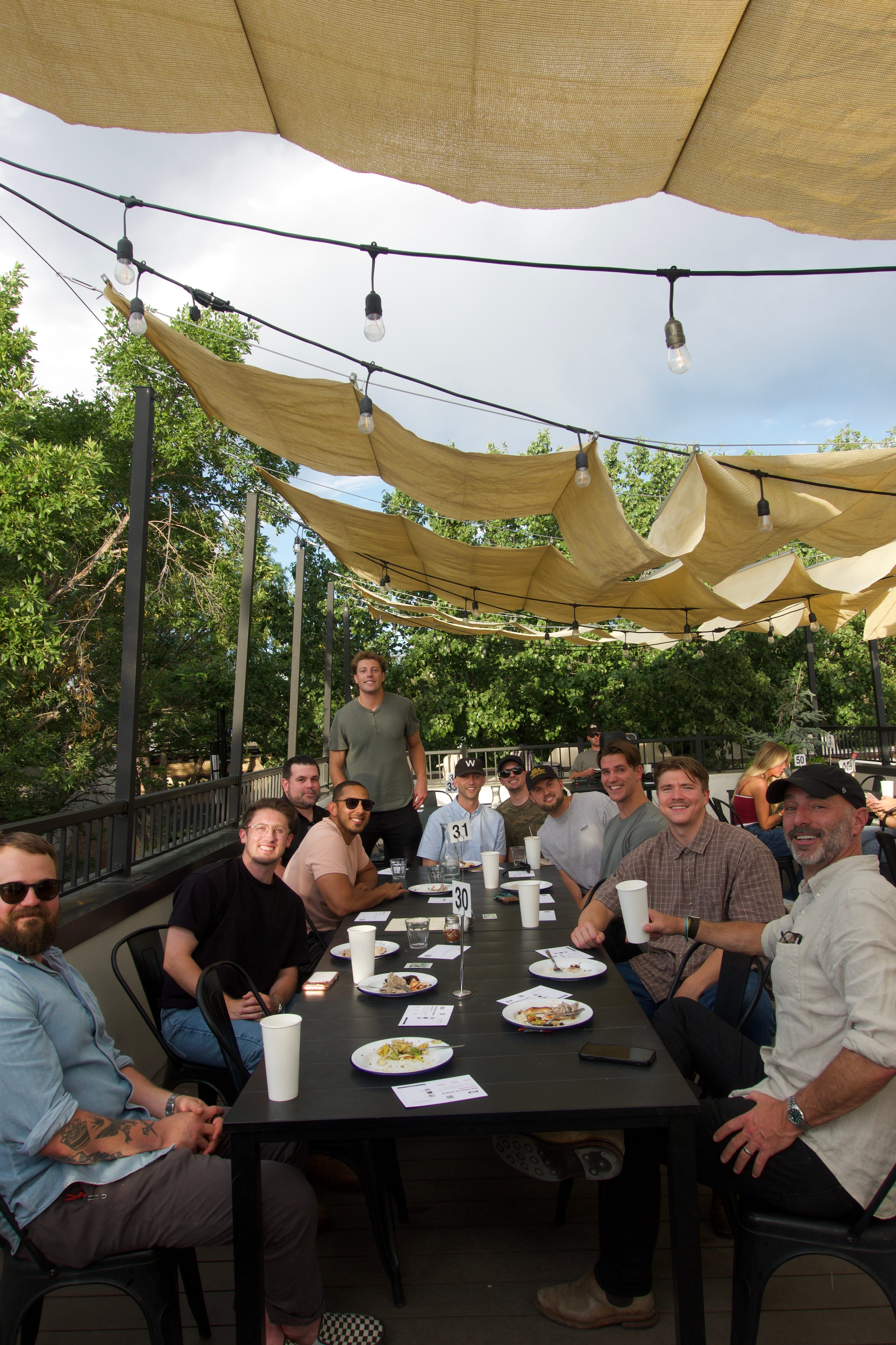 Long lunch table on a rooftop patio under shade sails and string lights