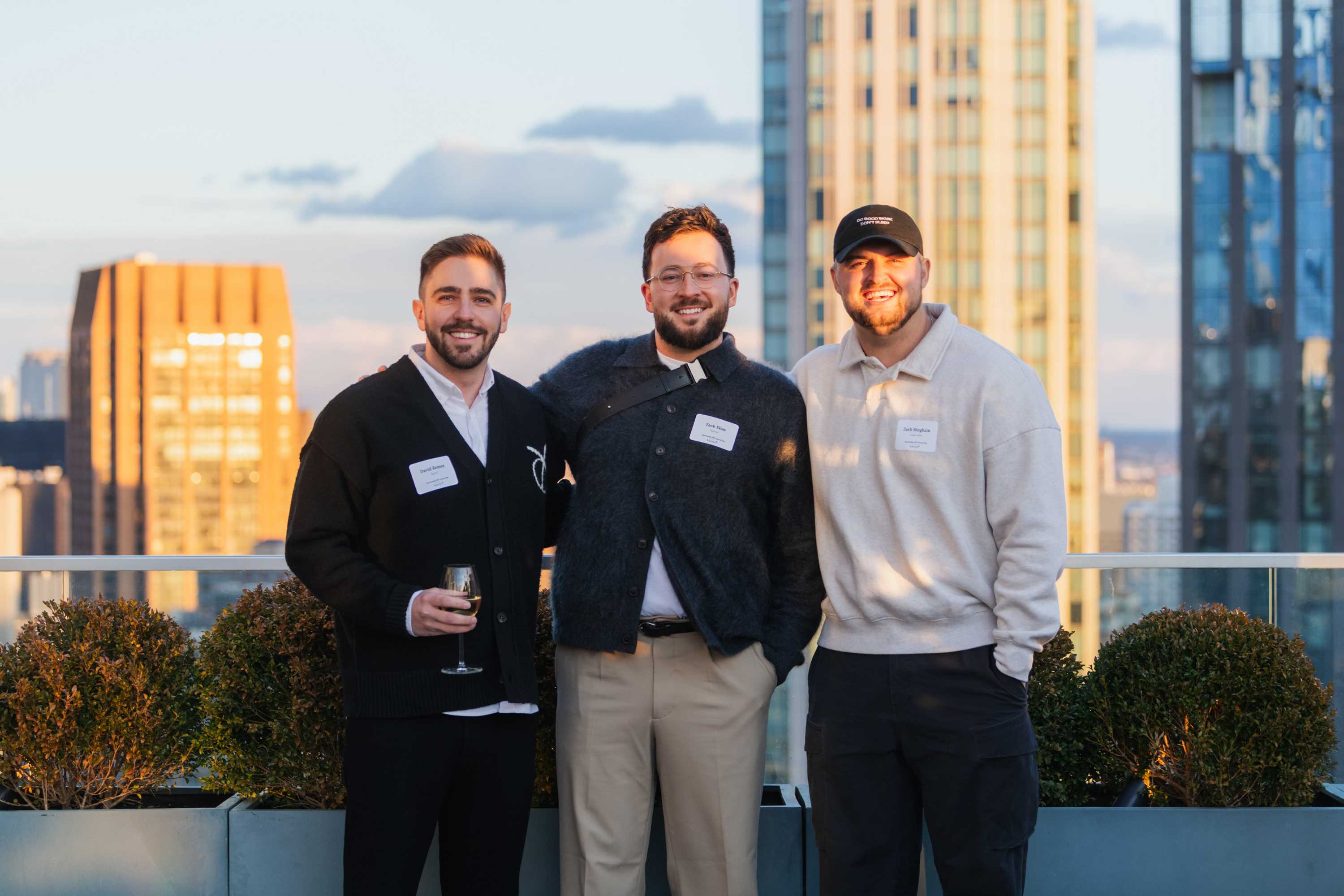 Three friends on a rooftop at sunset with city skyline and golden hour light