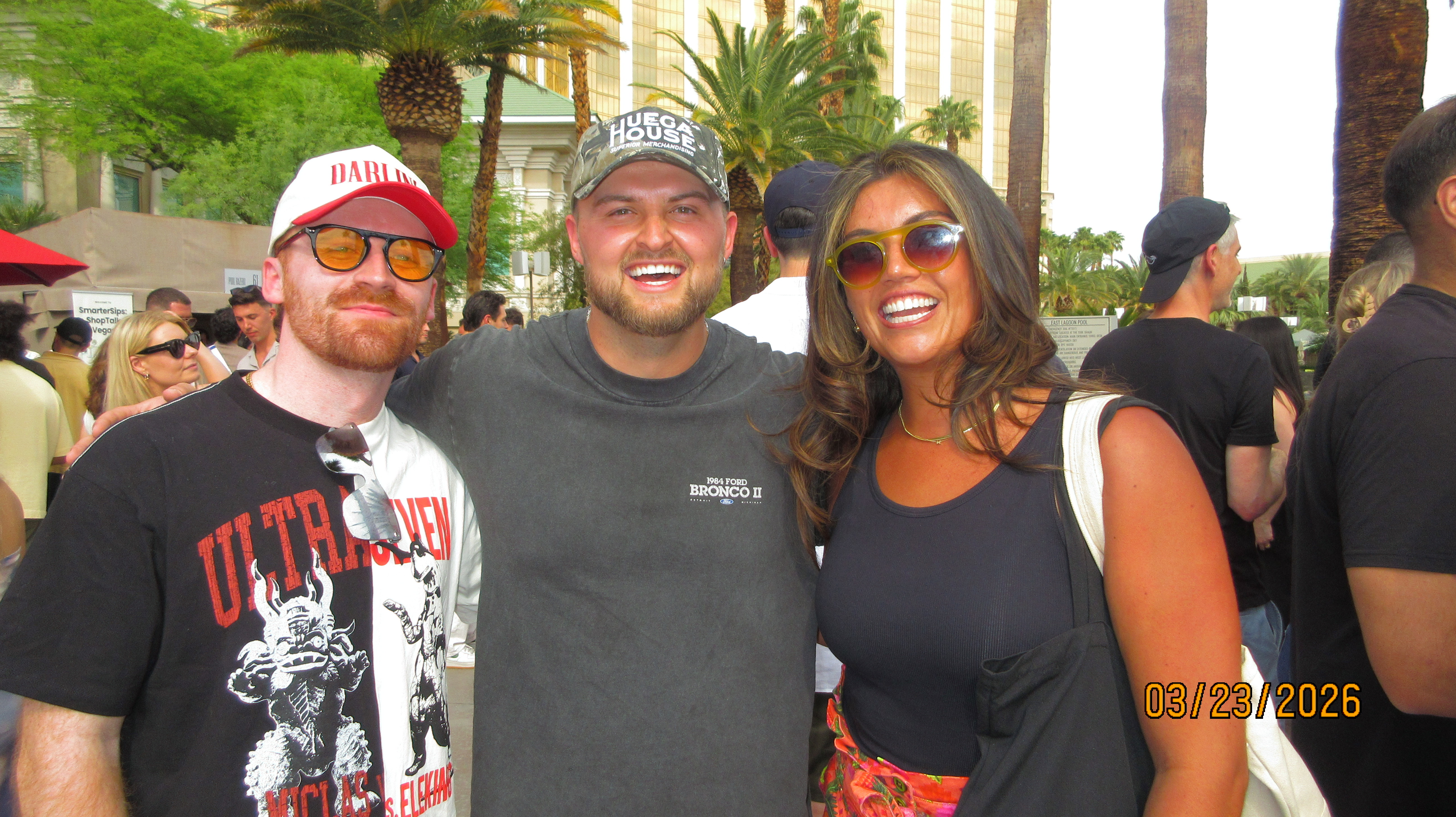 Three friends posing at a daytime Las Vegas pool party with palm trees and hotel tower behind